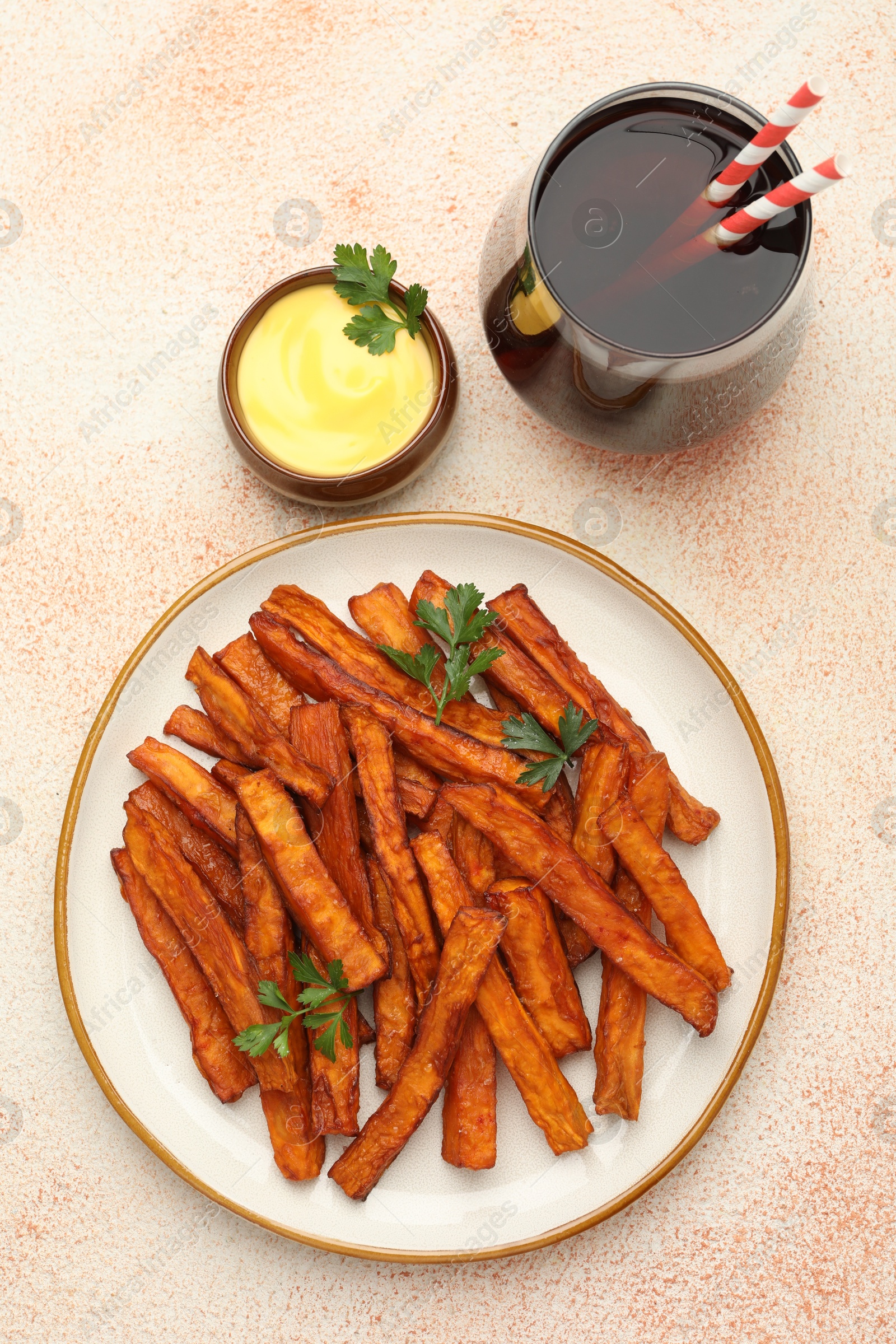 Photo of Delicious sweet potato fries, parsley, sauce and soda drink on beige textured table, top view