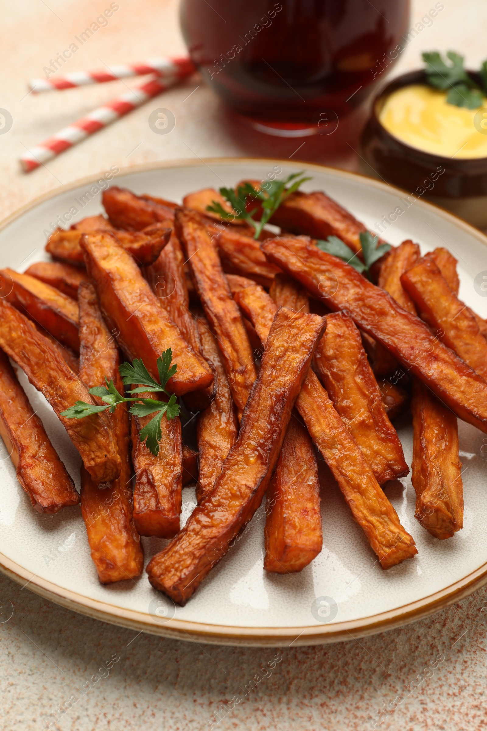 Photo of Delicious sweet potato fries, parsley and sauce on beige textured table, closeup