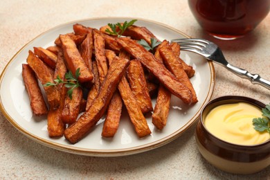 Delicious sweet potato fries, parsley and sauce on beige textured table, closeup