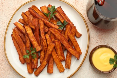 Photo of Delicious sweet potato fries, parsley, sauce and soda drink on beige textured table, top view