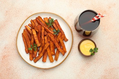 Photo of Delicious sweet potato fries, parsley, sauce and soda drink on beige textured table, top view