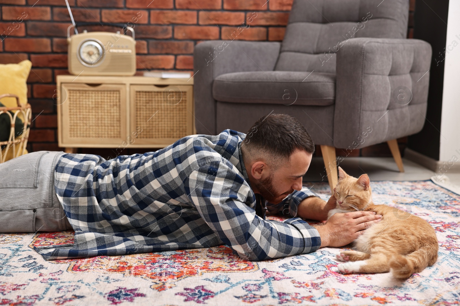 Photo of Man petting cute ginger cat on floor at home