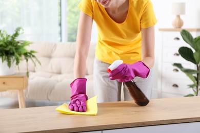 Woman cleaning table with rag and spray at home, closeup