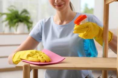 Young woman cleaning wooden shelf with rag and spray at home, closeup