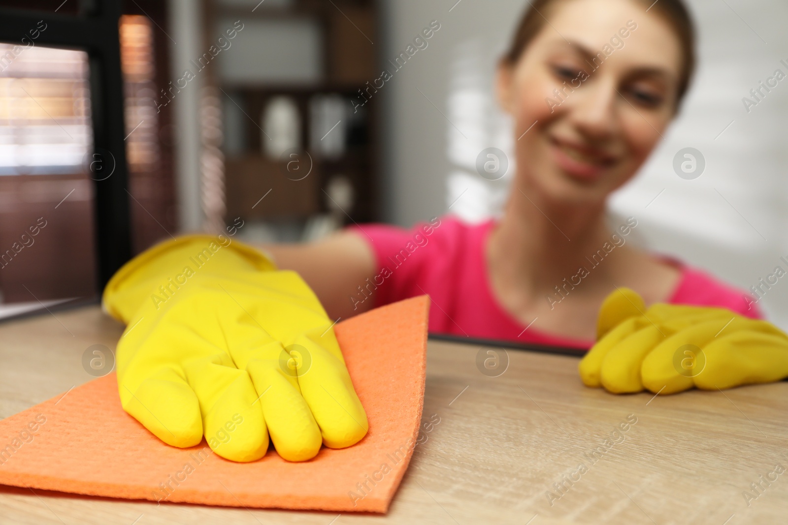 Photo of Young woman cleaning wooden shelf with rag in office, selective focus