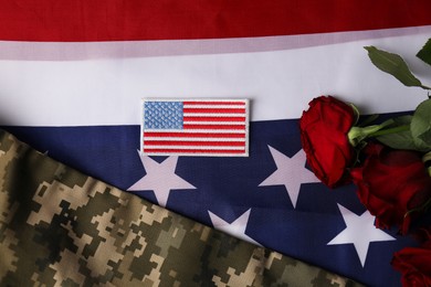 Photo of Veterans day. USA army patch, rose flowers and military uniform on American flag, flat lay