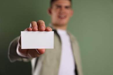 Photo of Man holding blank business card on green background, selective focus. Mockup for design