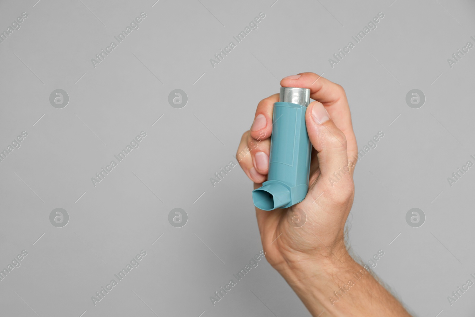 Photo of Man holding asthma inhaler on grey background, closeup. Space for text