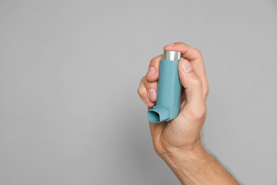 Man holding asthma inhaler on grey background, closeup. Space for text