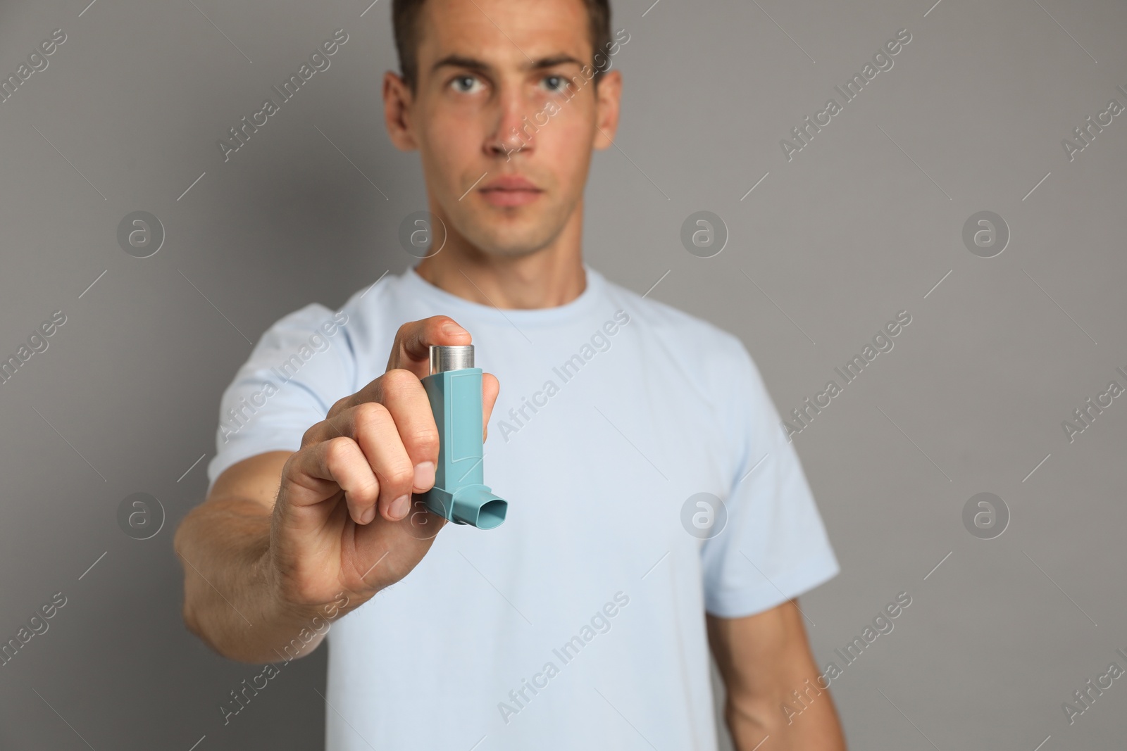 Photo of Man holding asthma inhaler on grey background, selective focus