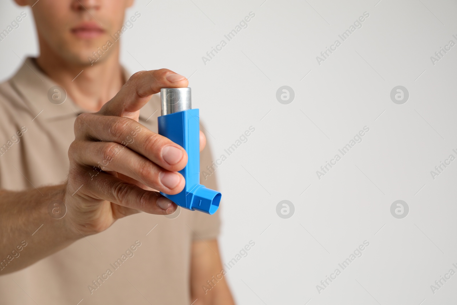 Photo of Man holding asthma inhaler on light background, closeup. Space for text