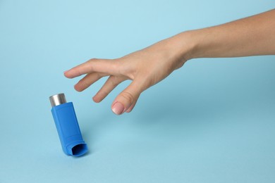 Woman reaching for asthma inhaler on light blue background, closeup