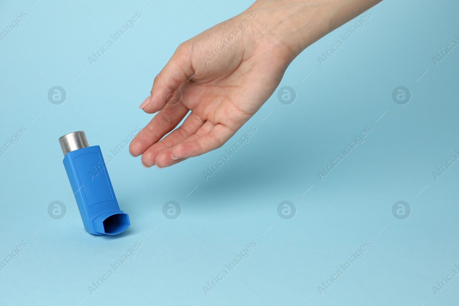 Photo of Woman reaching for asthma inhaler on light blue background, closeup. Space for text