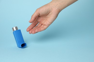 Woman reaching for asthma inhaler on light blue background, closeup. Space for text