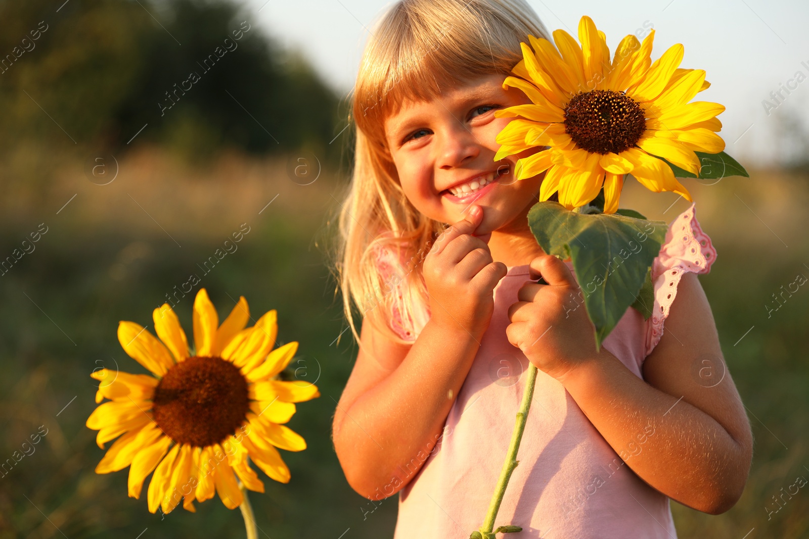 Photo of Little girl with sunflowers at meadow. Child enjoying beautiful nature