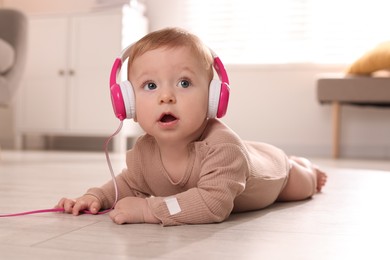 Photo of Cute little baby with headphones on floor at home