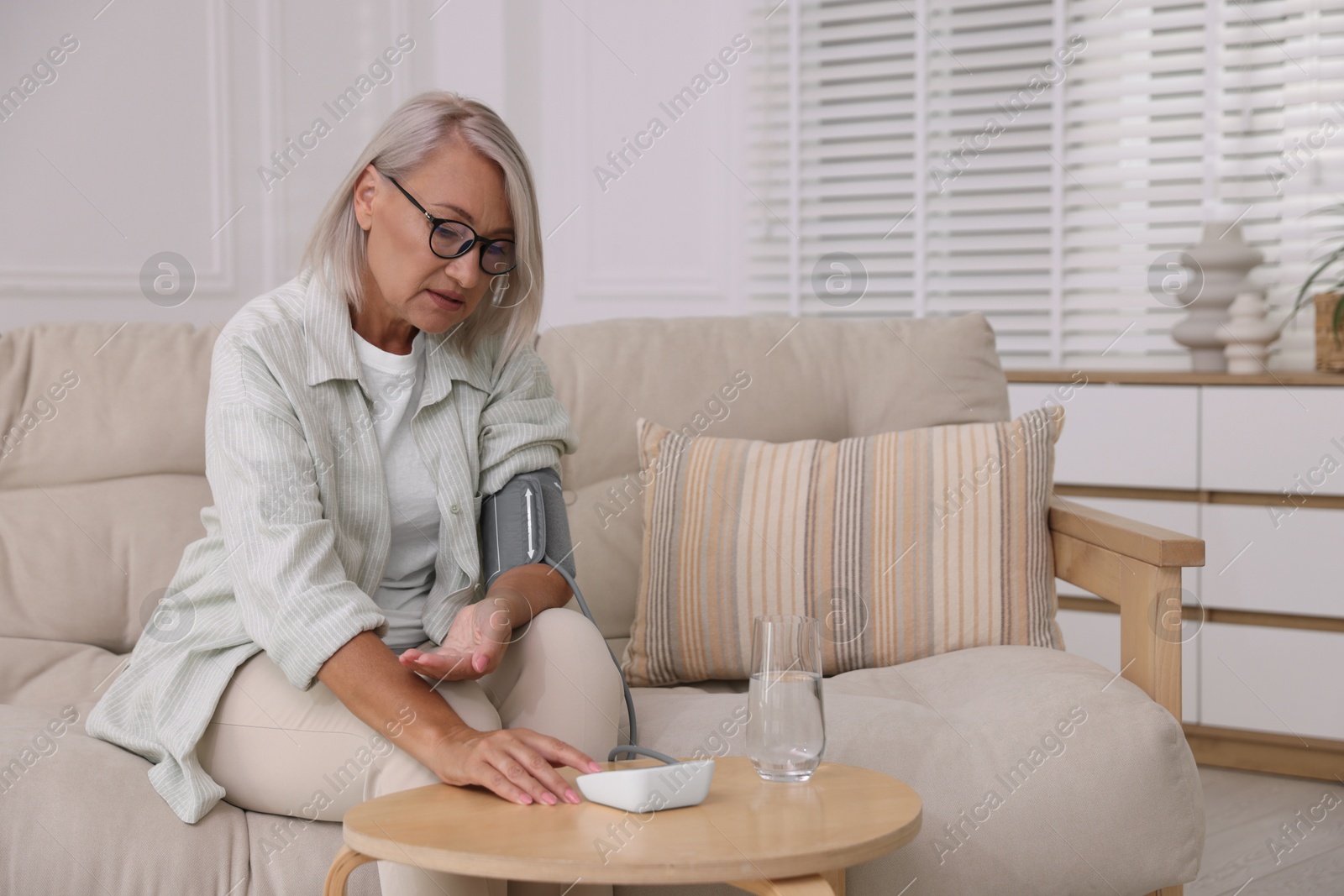 Photo of Woman measuring blood pressure on sofa indoors