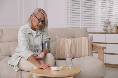 Woman measuring blood pressure on sofa indoors