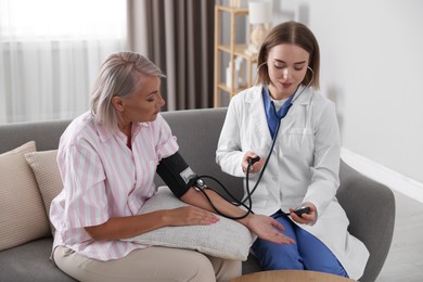 Doctor measuring patient's blood pressure on sofa indoors