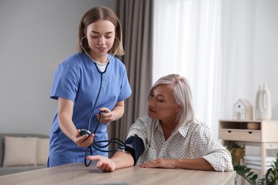 Healthcare worker measuring patient's blood pressure at wooden table indoors