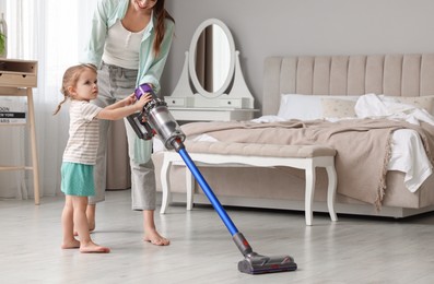 Young woman and her daughter cleaning floor with cordless vacuum cleaner in bedroom, closeup