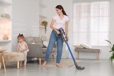 Smiling young woman and her daughter cleaning floor with cordless vacuum cleaner at home