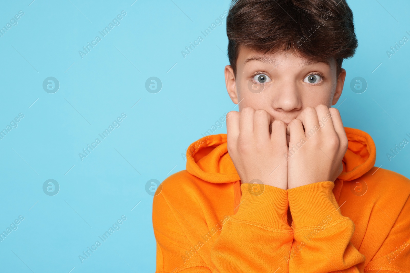 Photo of Scared teenage boy on light blue background. Space for text