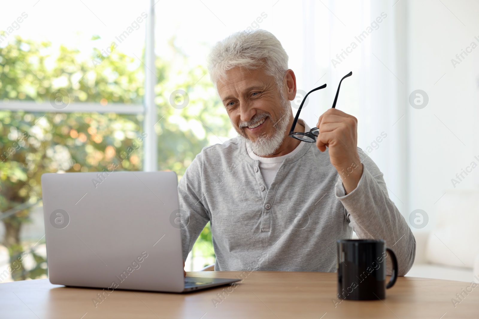 Photo of Senior man with glasses using laptop at table indoors