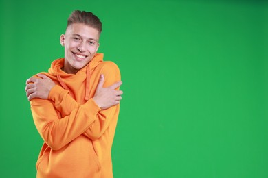 Young man hugging himself on green background, space for text