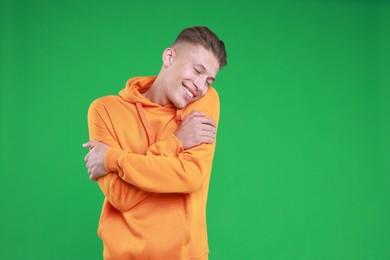 Young man hugging himself on green background, space for text