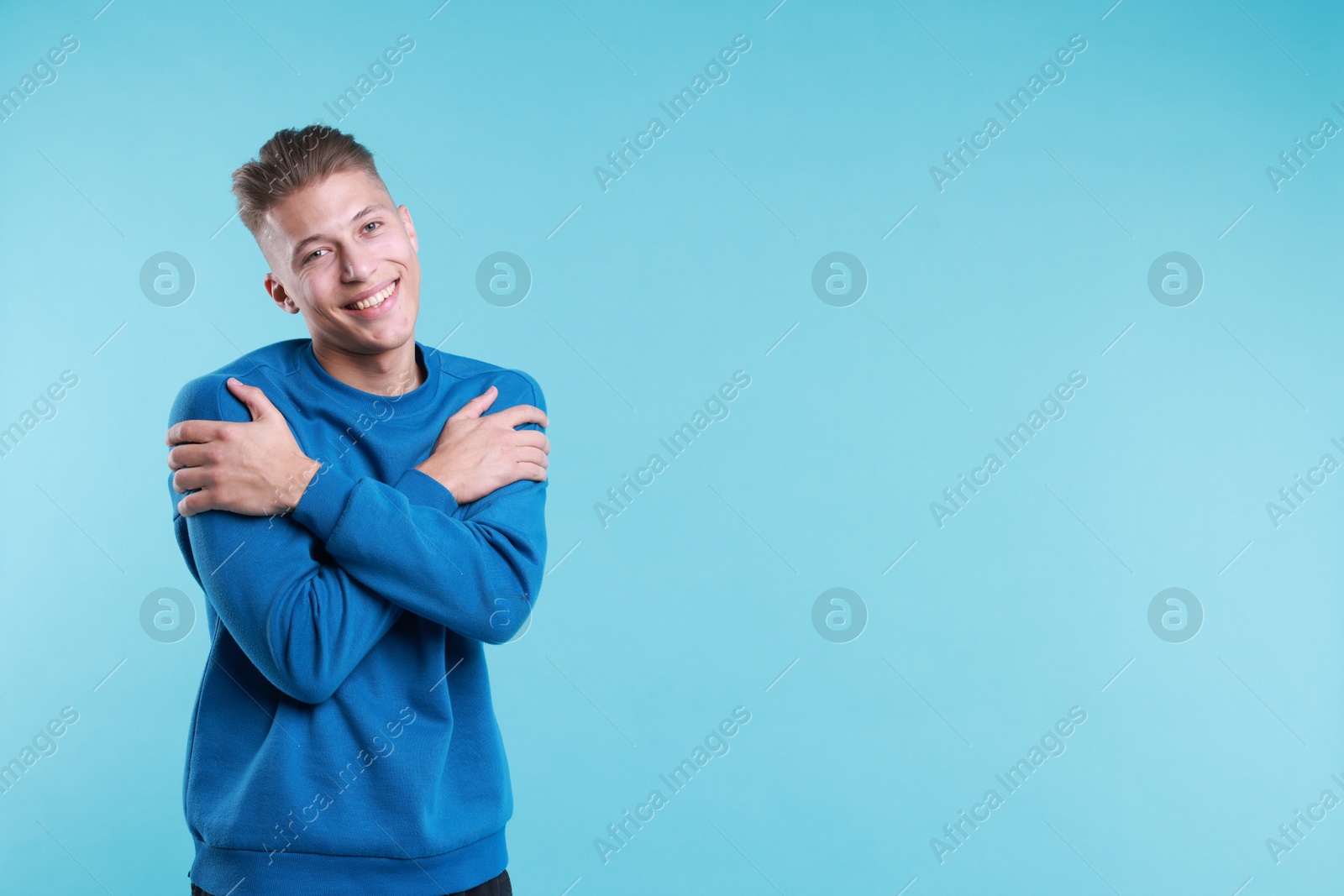 Photo of Young man hugging himself on light blue background, space for text