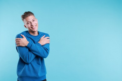 Photo of Young man hugging himself on light blue background, space for text