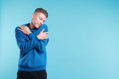 Young man hugging himself on light blue background, space for text