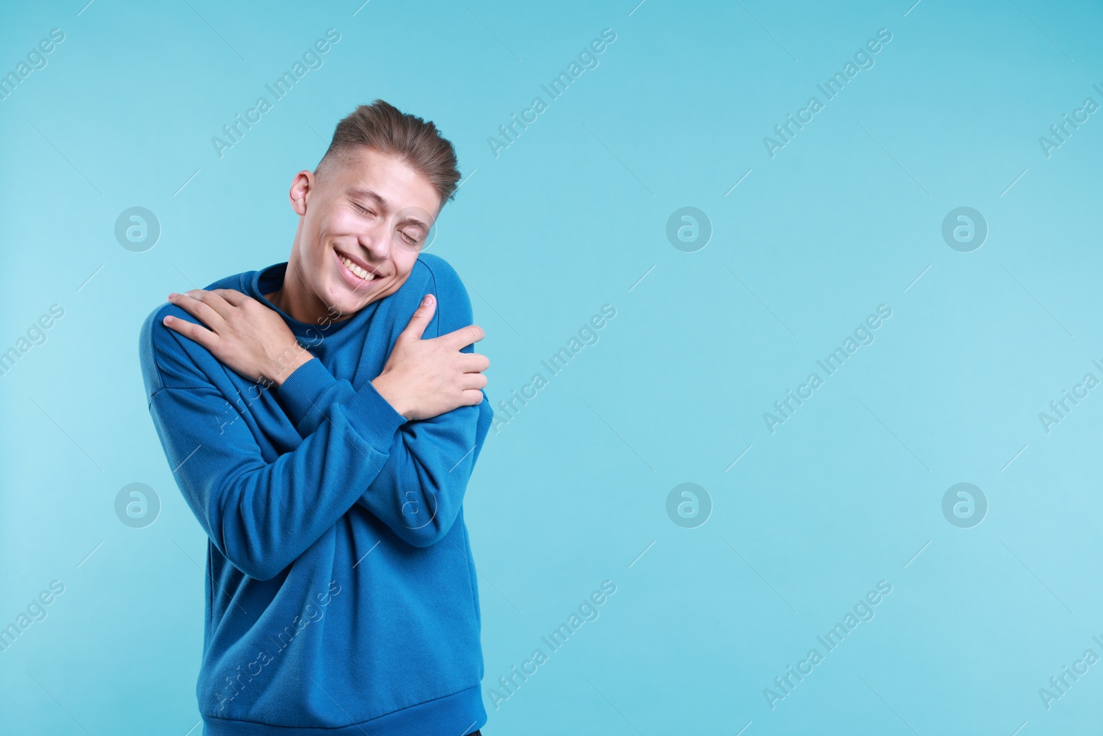 Photo of Young man hugging himself on light blue background, space for text