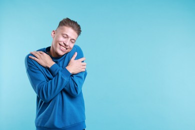 Photo of Young man hugging himself on light blue background, space for text