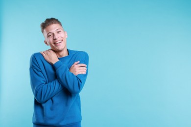 Young man hugging himself on light blue background, space for text