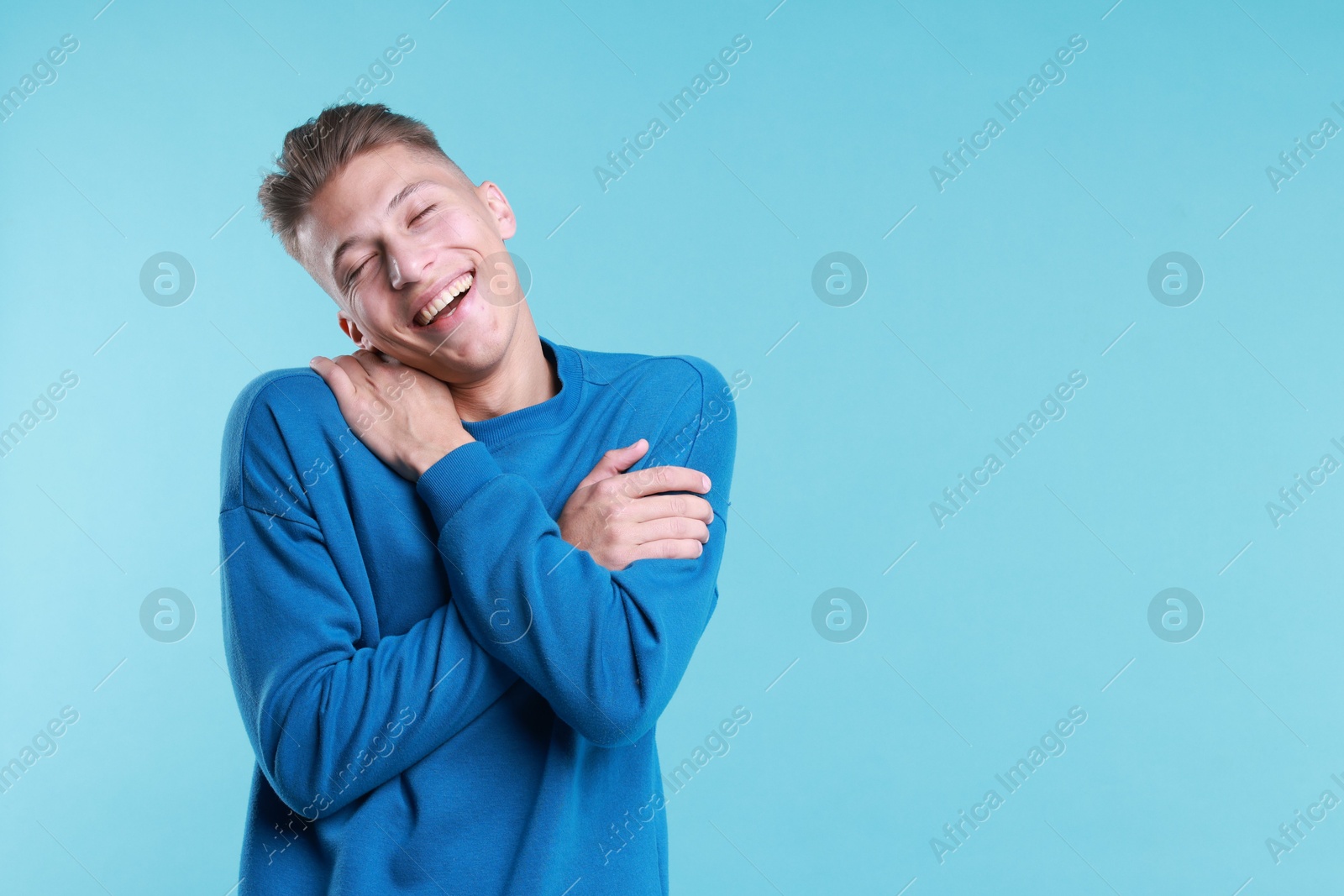 Photo of Young man hugging himself on light blue background, space for text