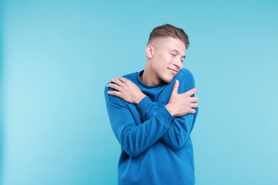 Young man hugging himself on light blue background