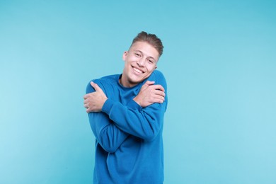 Young man hugging himself on light blue background