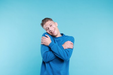 Young man hugging himself on light blue background