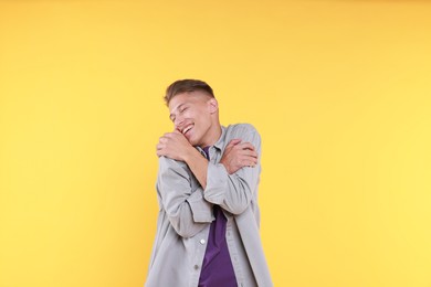 Young man hugging himself on yellow background