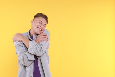 Photo of Young man hugging himself on yellow background, space for text