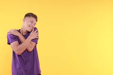 Young man hugging himself on yellow background, space for text