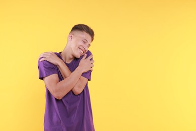 Young man hugging himself on yellow background, space for text