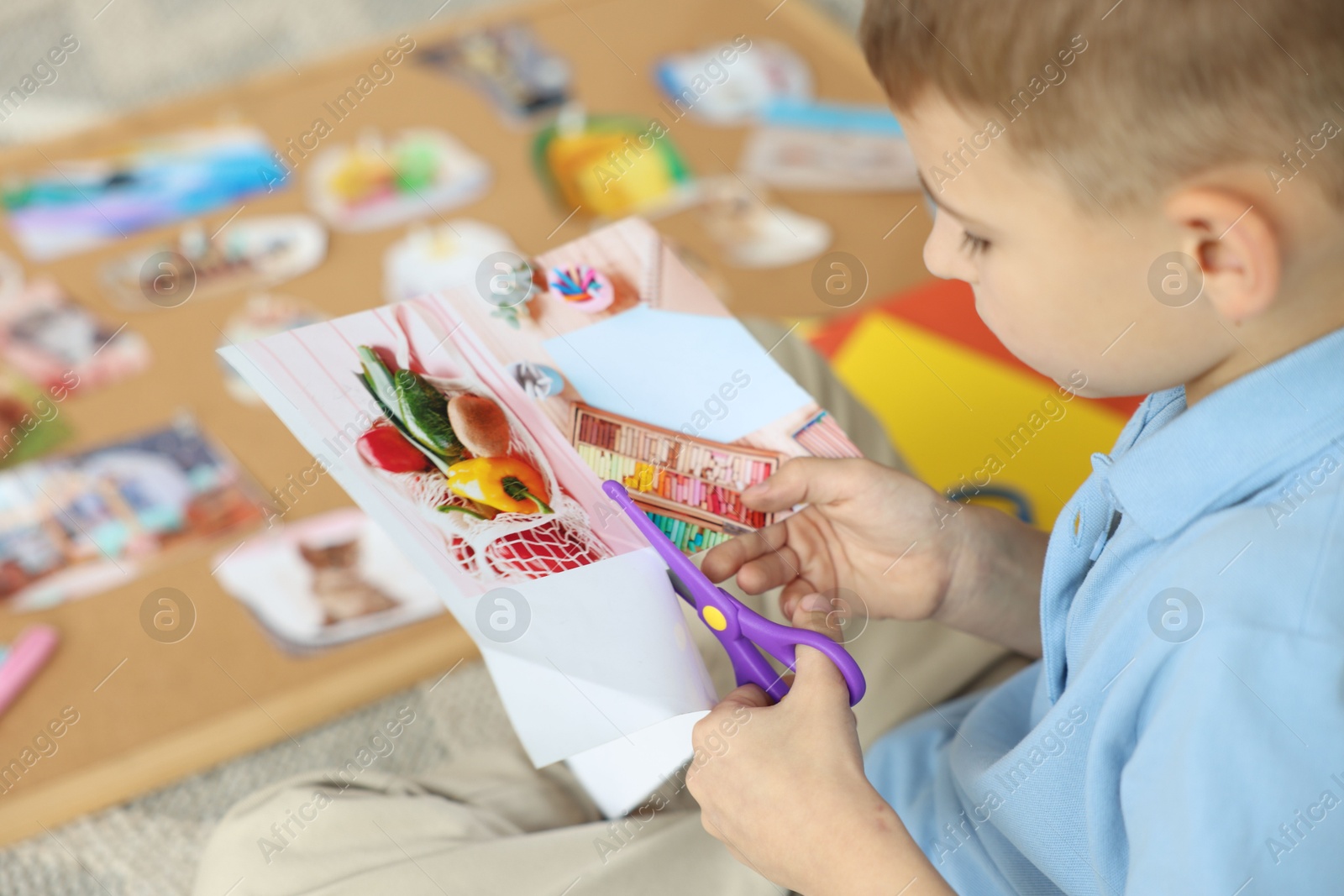 Photo of Creating vision board. Little boy cutting out picture on floor indoors