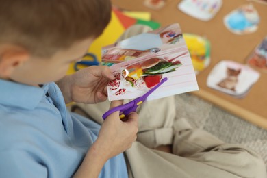 Creating vision board. Little boy cutting out picture on floor indoors