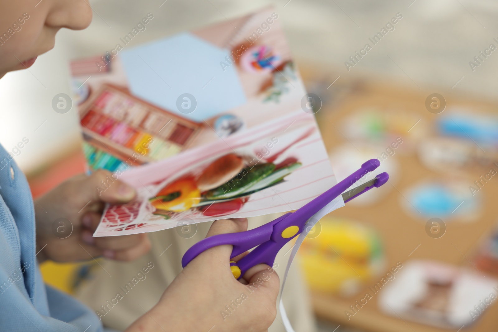 Photo of Creating vision board. Little boy cutting out picture indoors, closeup