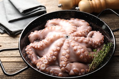 Fresh raw octopus and thyme in frying pan on wooden table, closeup