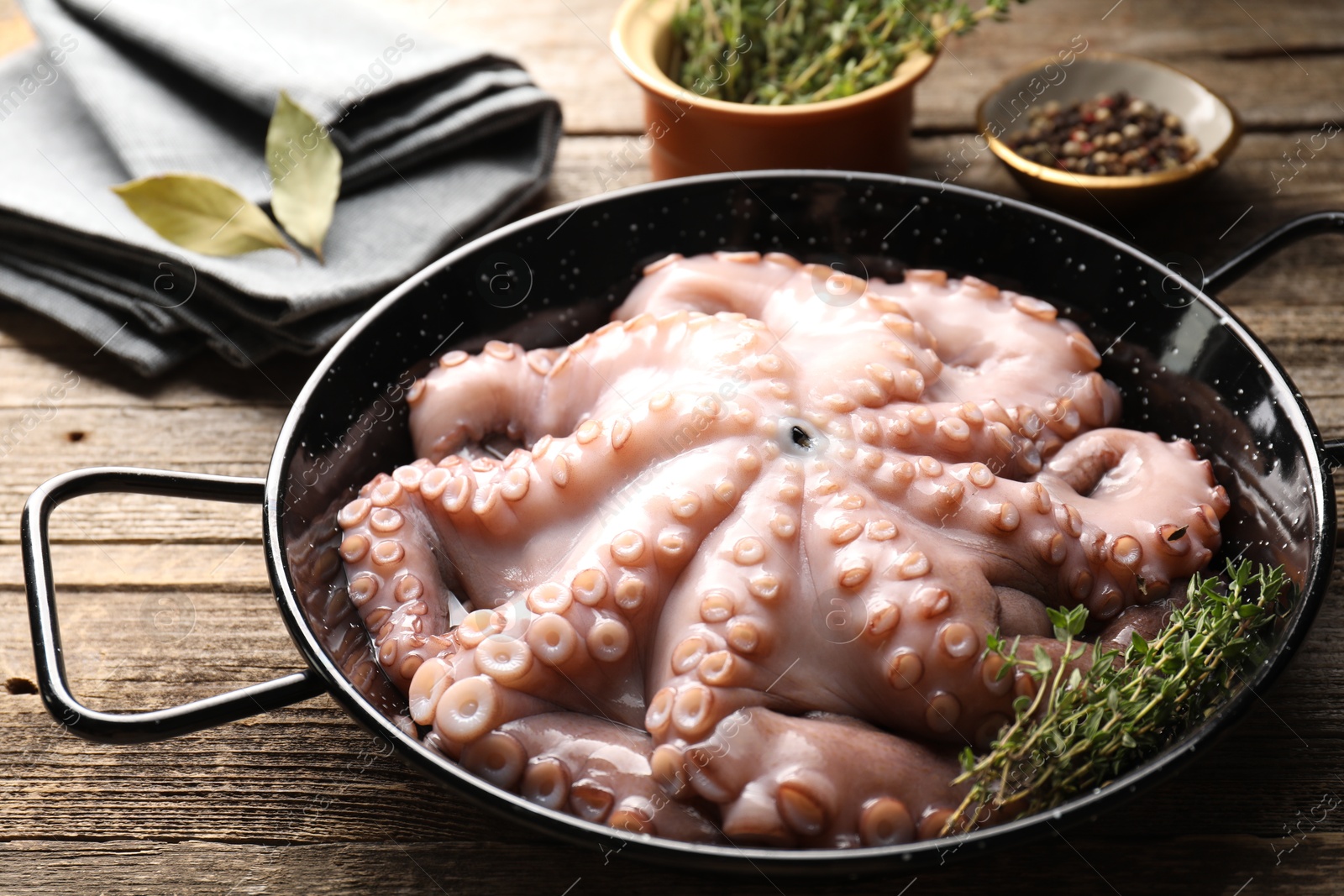 Photo of Fresh raw octopus and thyme in frying pan on wooden table, closeup