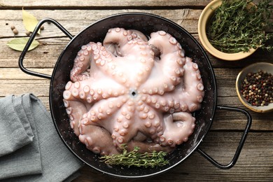 Photo of Fresh raw octopus and thyme in frying pan on wooden table, top view